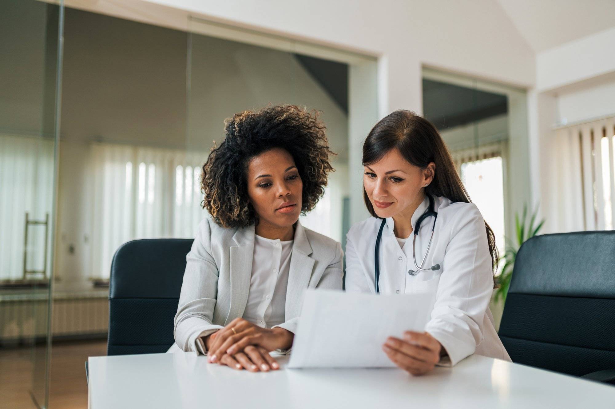 General practitioner showing test results to a charming mixed race woman. General practitioner showing test results to a charming mixed race woman.