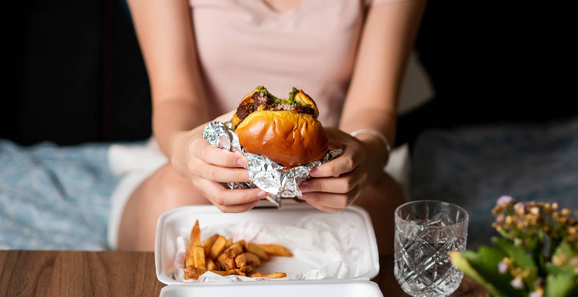 Woman eating burger and fries delivered at home alone