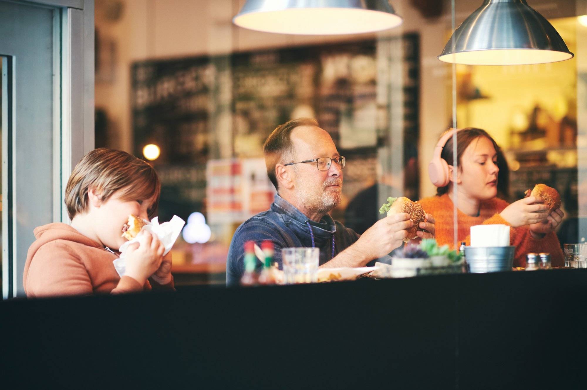 Family lunch, father with children eating hamburgers, in restaurant, sitting by the window Family lunch, father with children eating hamburgers, in restaurant, sitting by the window