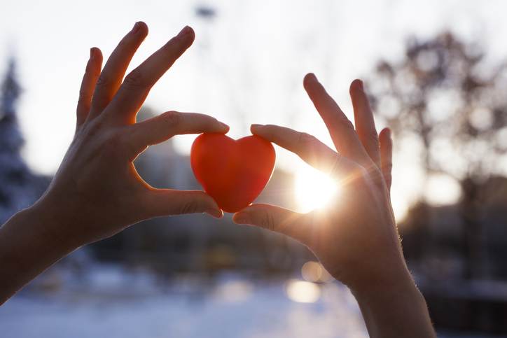 Woman hands holding red heart at sunset